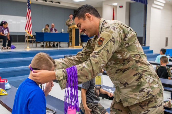 Military Airman puts purple necklace around student for Month of the Military Child.