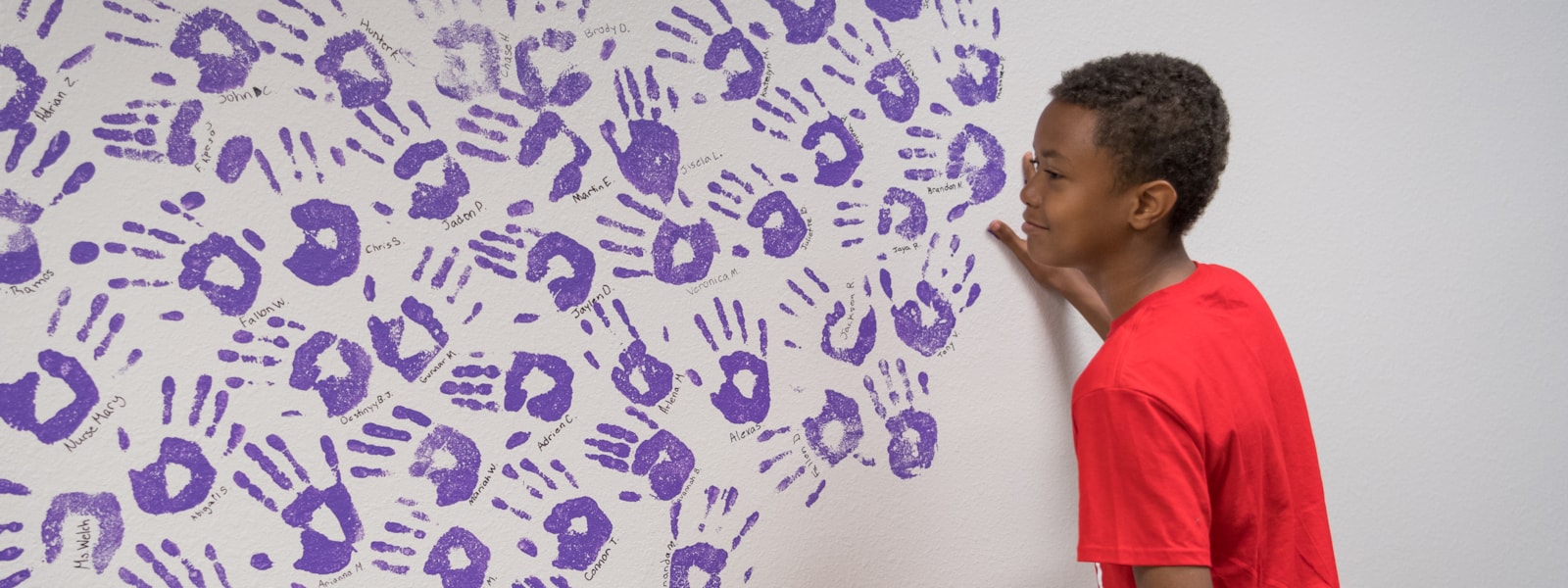 An african american male student putting his handprint on a mural of other handprints