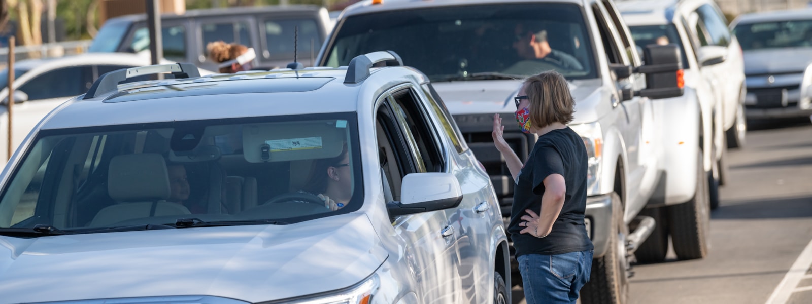 staff member waving while talking to a parent in their vehicle