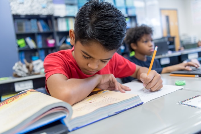 boy working in classroom with book and notes