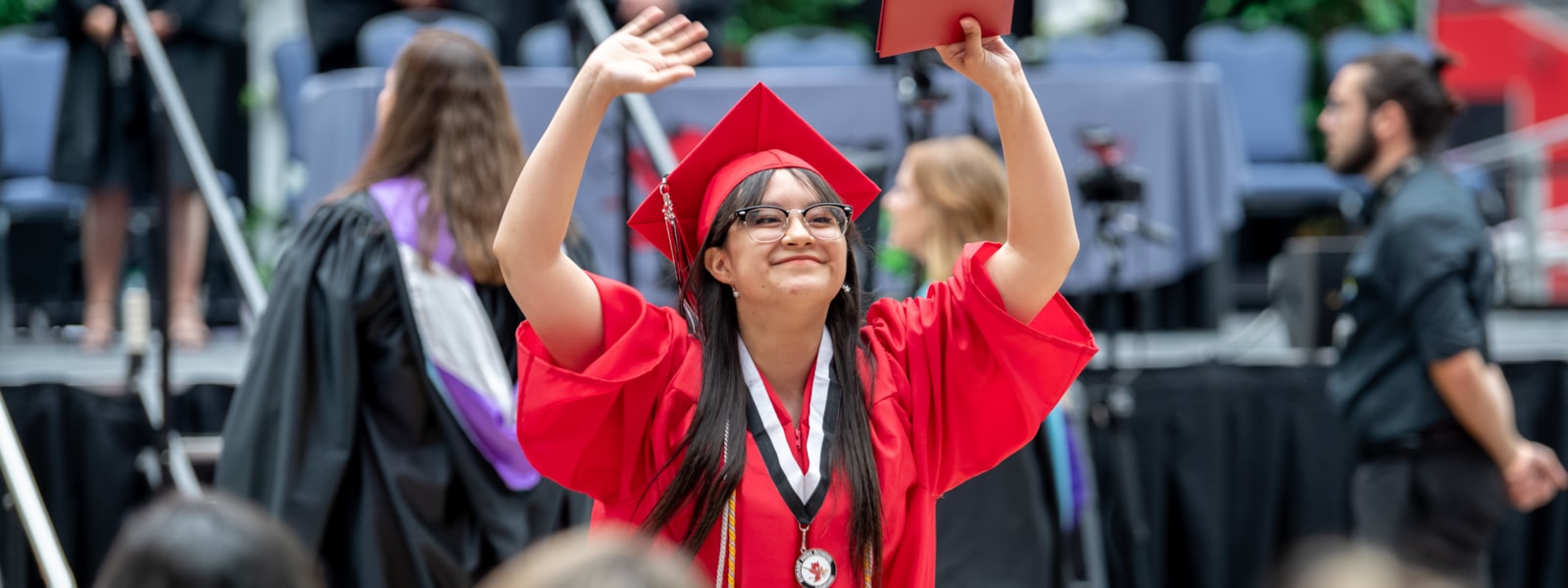 A Dysart Senior at graduation holding her diploma up, walking back to her seat. 