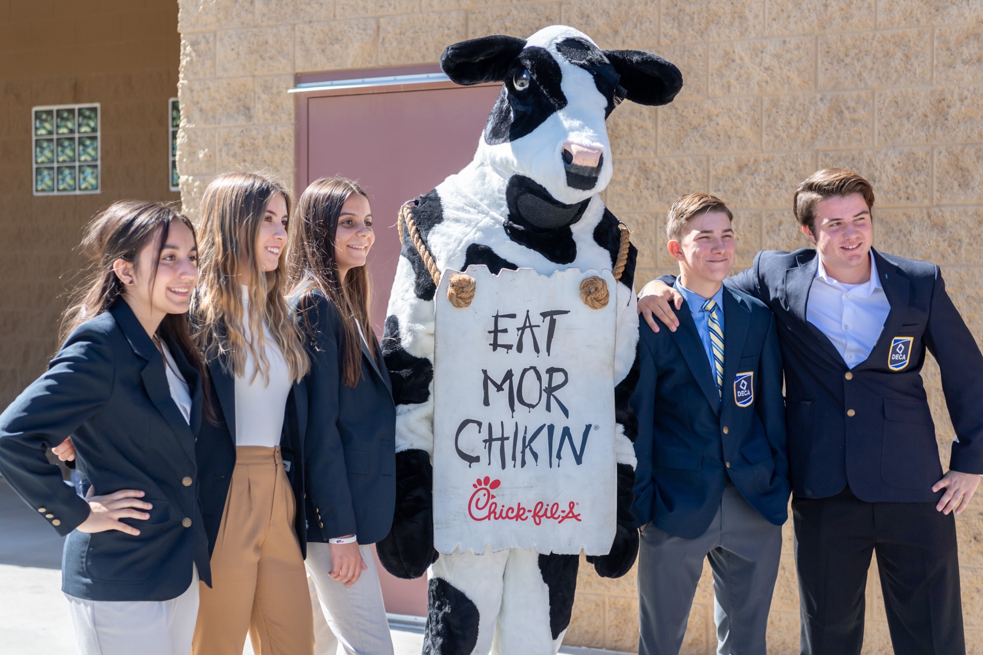 Marketing students wearing DECA coats posing with a cow mascot