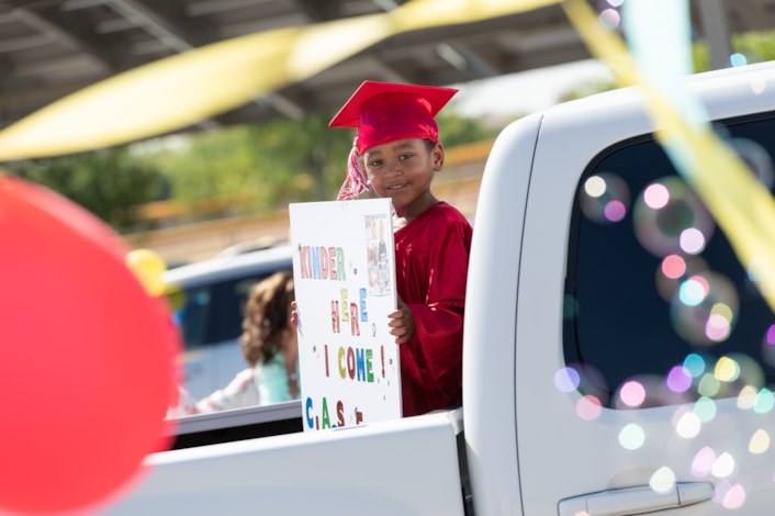 preschool graduate holding sign with balloons