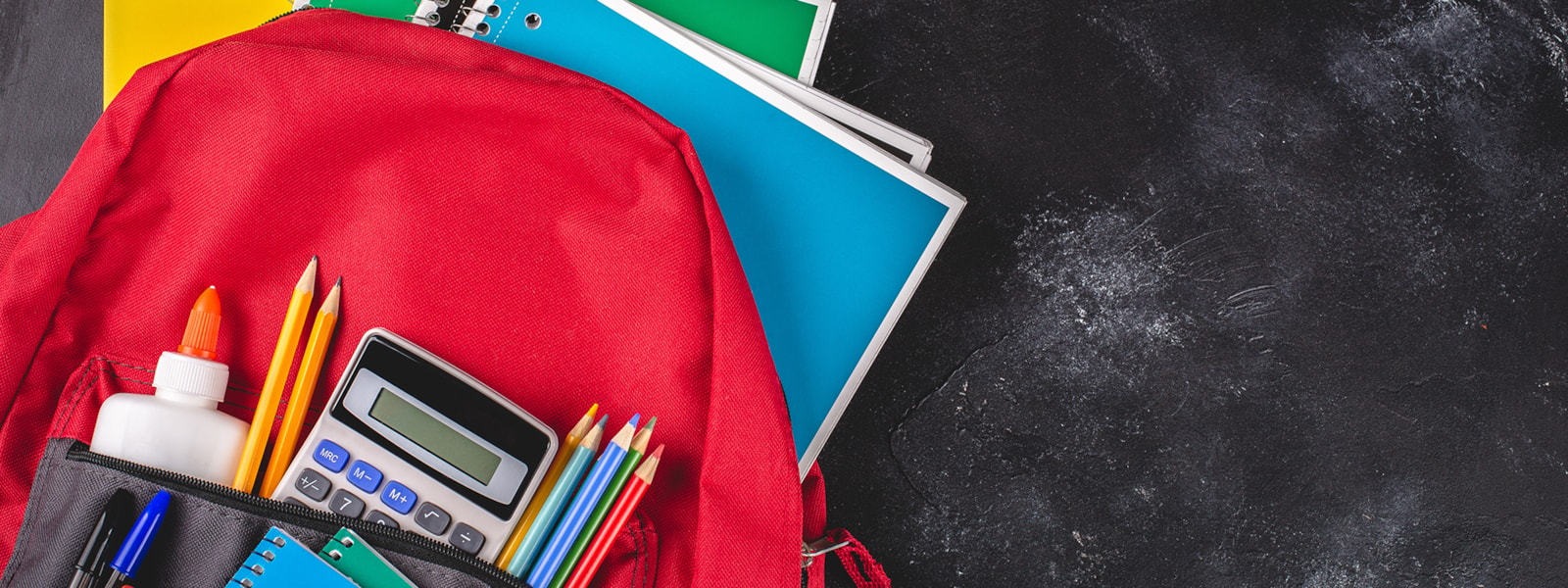 Red backpack with calculator, notebooks, pencils, and a glue bottle