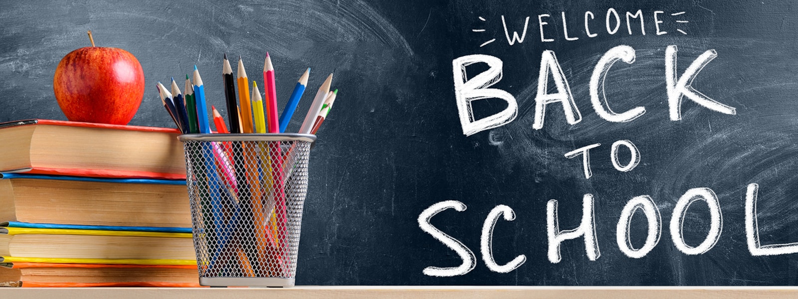 Welcome back to school sign on a chalkboard with a an apple, books and pencils next to it.