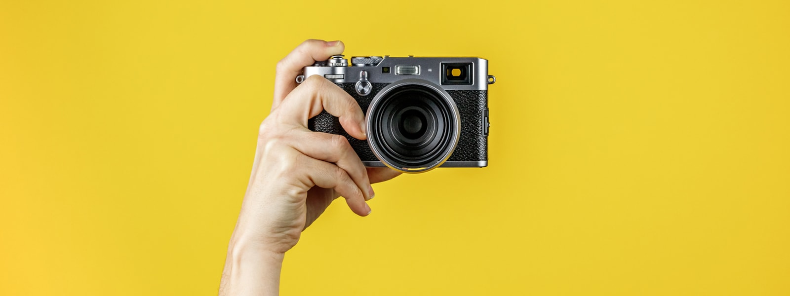 hand holding a camera in front of a yellow background