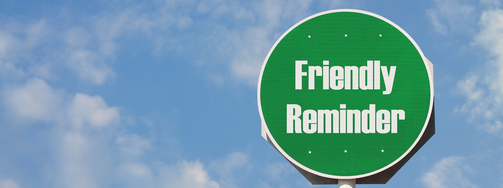 Green sign with words "Friendly Reminder" against sky background
