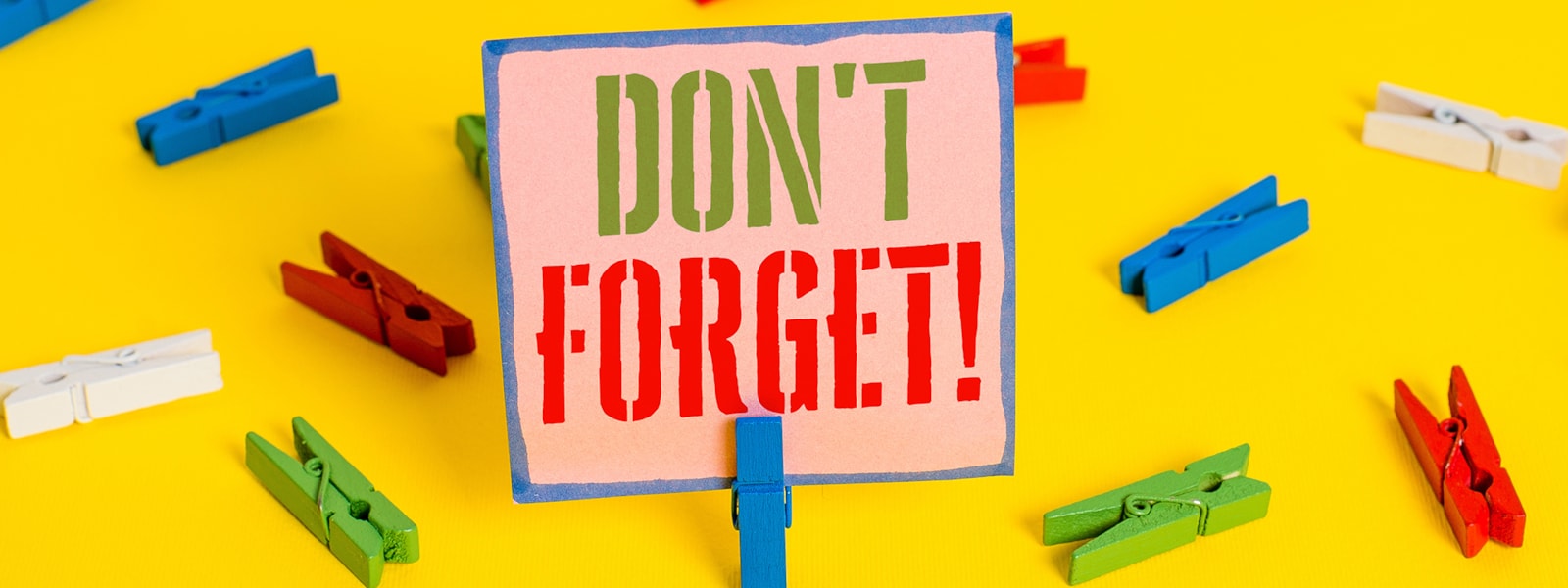 "Don't forget" sign in front of colorful clothes pins. 