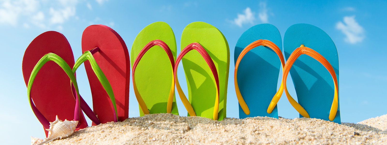 colorful flip flop shoes in the sand with a blue sky in the background