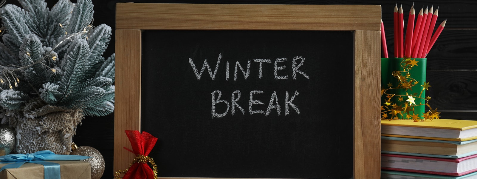 A chalk board sign with the words Winter Break on it with school supplies and holiday items around it.