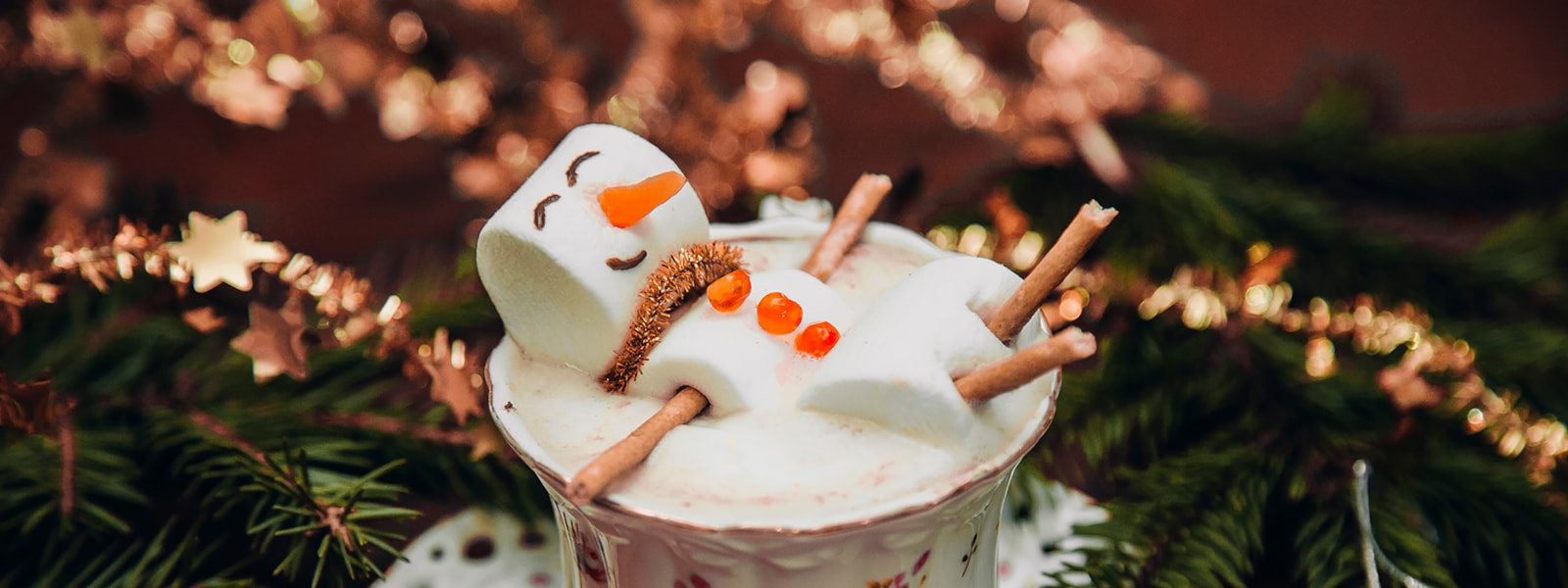 snowman made out of marshmallows floating in a cup of hot cocoa, branches around it 