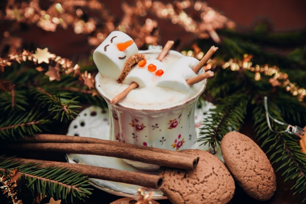 snowman made out of marshmallows floating in a cup of hot cocoa, branches around it 