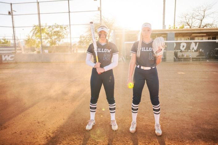 Two softball players standing on field posing for camera.
