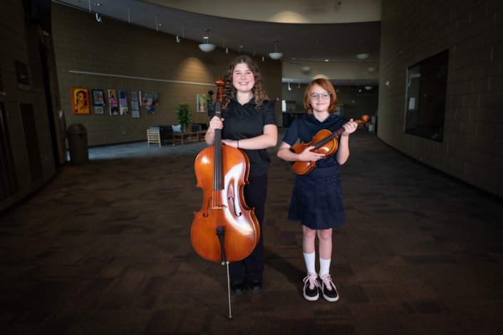 Two girls with orchestra instruments posing for camera