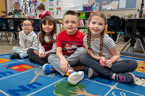 Kindergarten students sitting on rug in classroom smiling