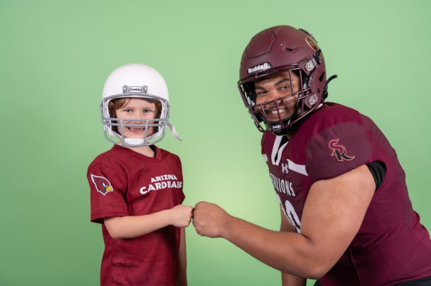 Two students dressed as football players fist bump while smiling for camera.