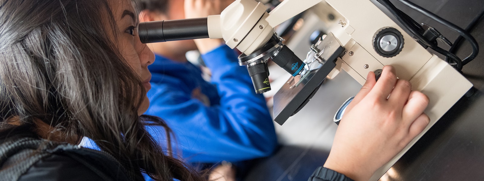 High school student looks through a microscope in a science class.