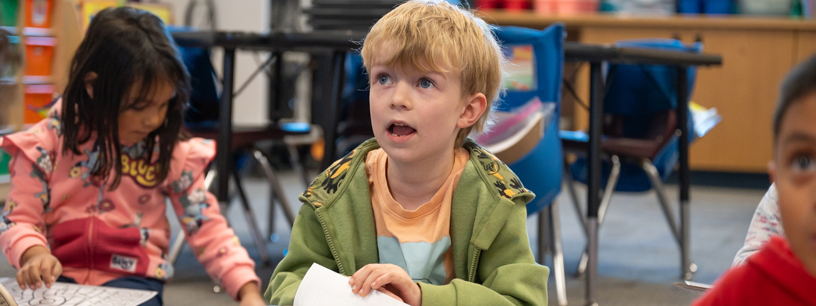 Kindergarten student sitting on the rug and looking up at his teacher