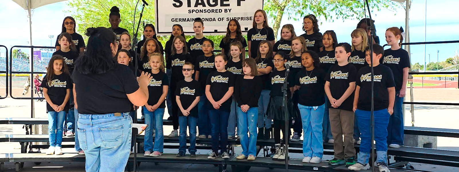 Choir students wearing Falcons shirts standing on risers outside performing at the Festival of the Arts