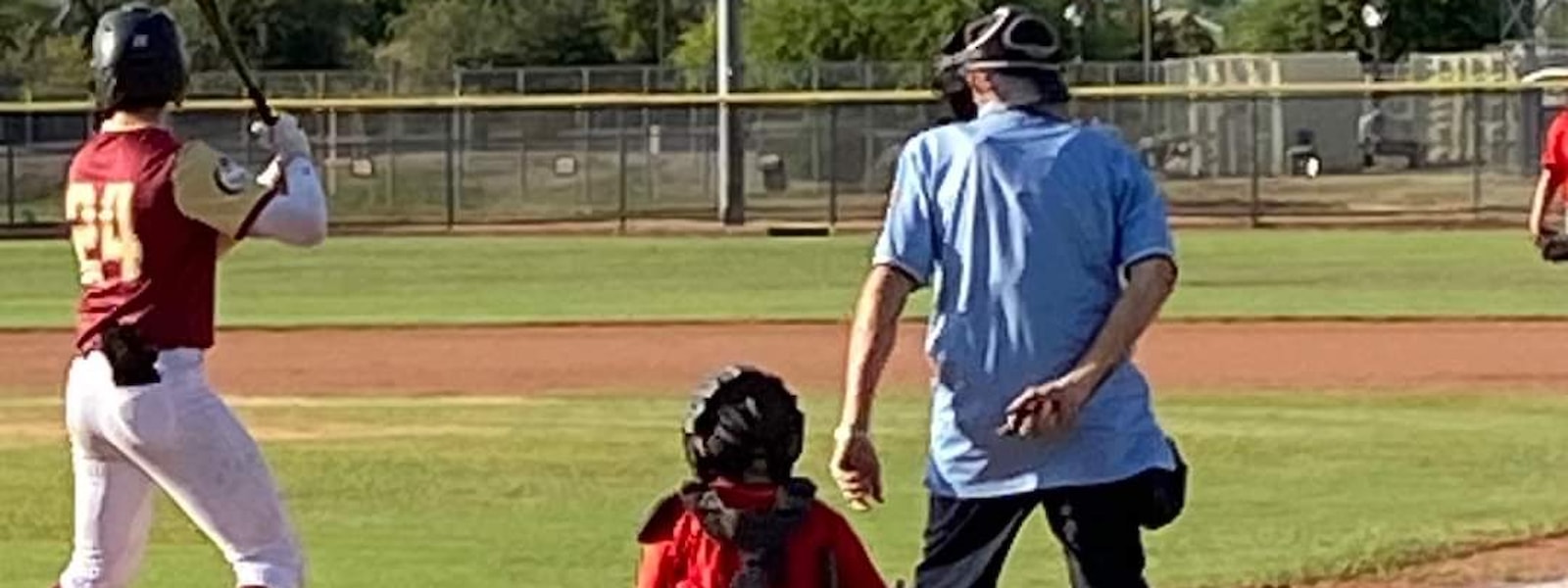 Boy playing catcher kneeling by umpire while a player is at bat