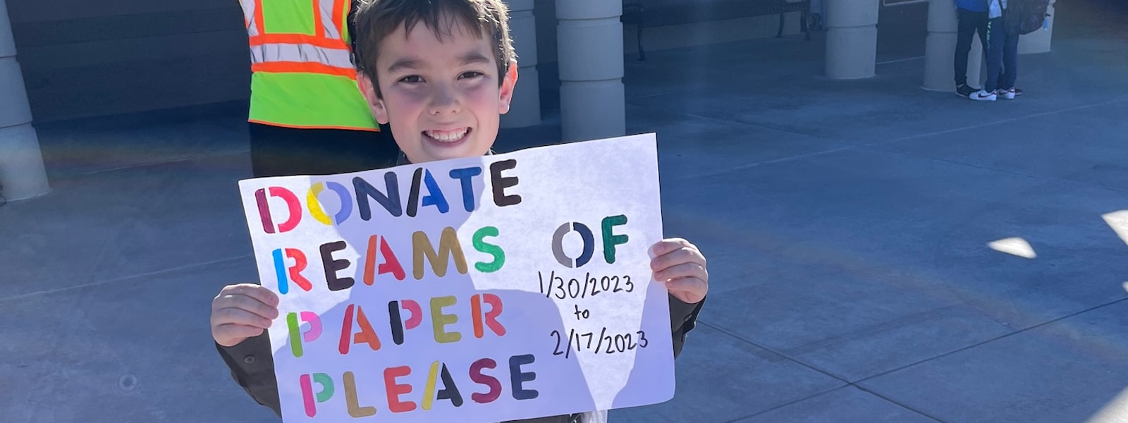 Student holding sign asking to donate paper