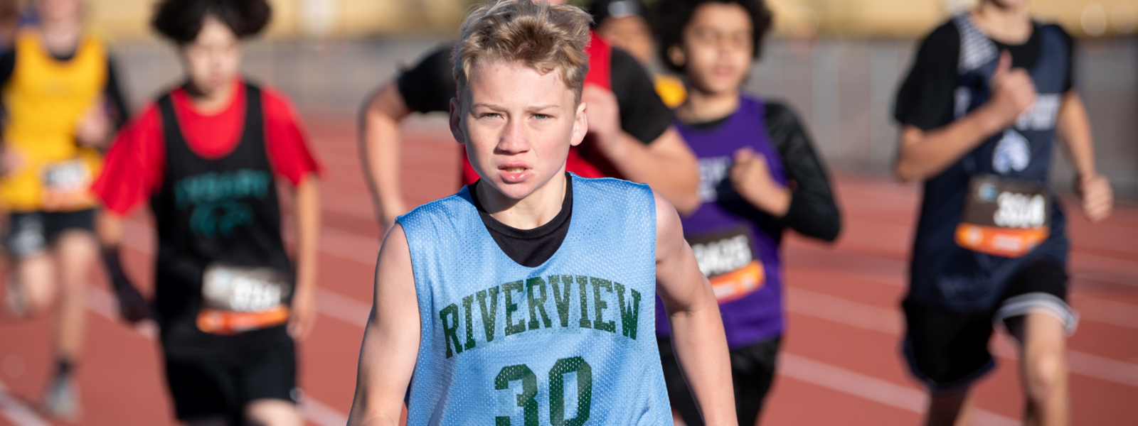 Student in Riverview cross country uniform running towards the camera with students form other schools blurred in that background