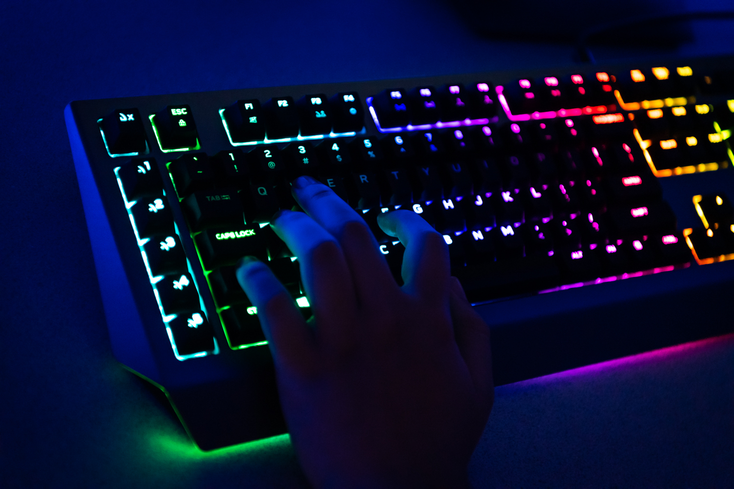 A hand is seen on a lit keyboard as a student plays an esport game