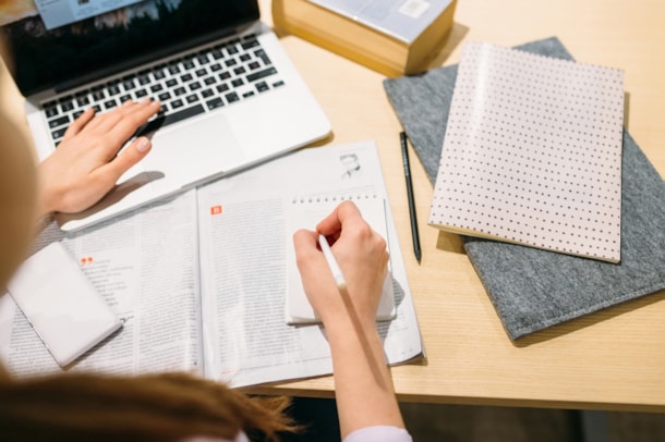 student writing on desk with computer and books