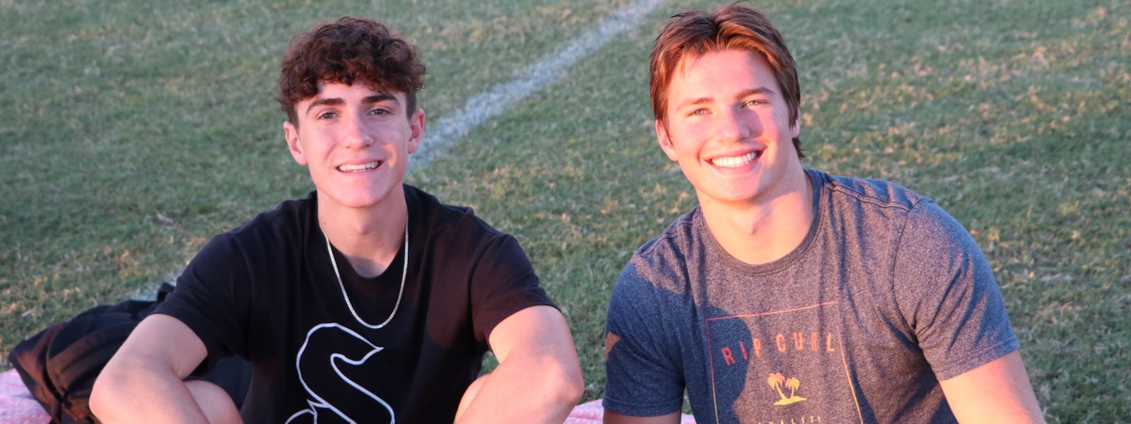 Two male students sitting on the football field