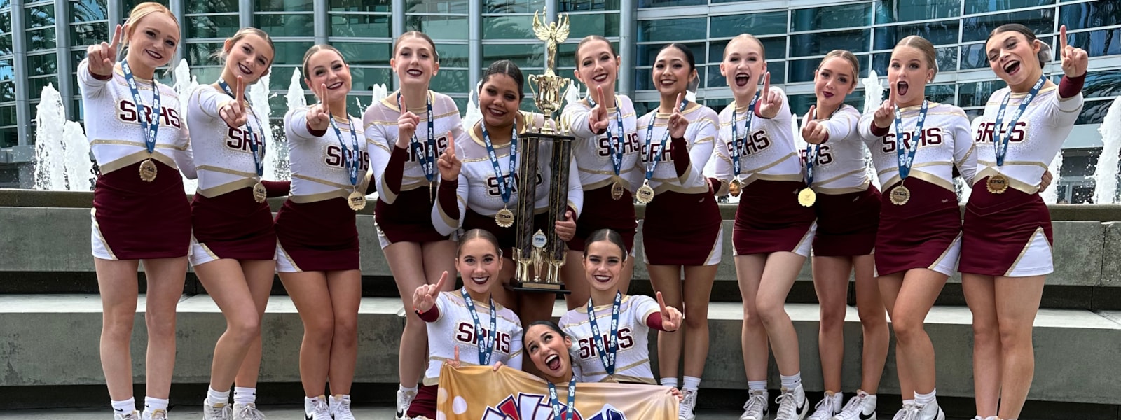 Pom team wearing medals and holding a trophy