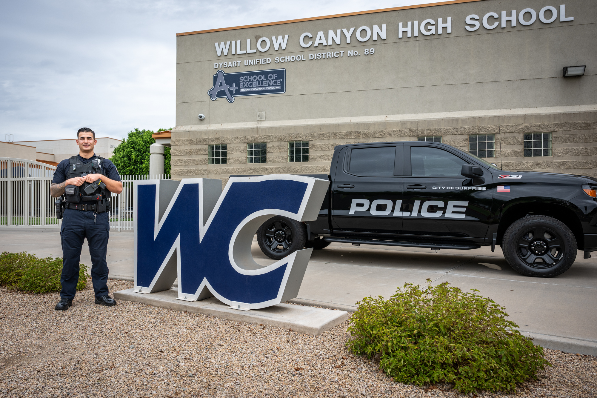 Smiling officer in front of police truck with school building in the background.